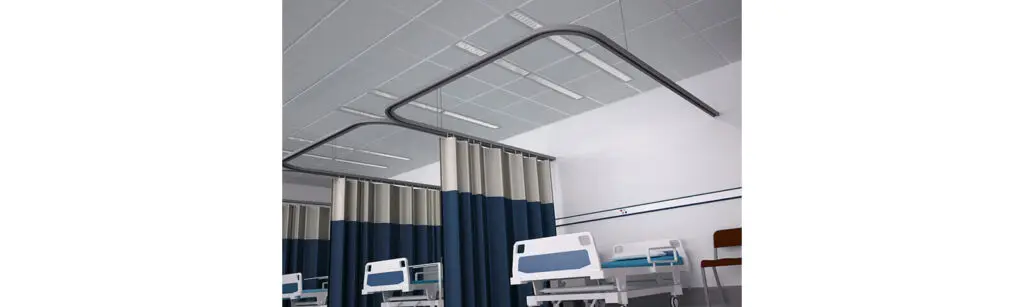 Hospital ward with beds, privacy curtains, and overhead linear LED lighting.