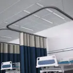 Hospital ward with beds, privacy curtains, and overhead linear LED lighting.